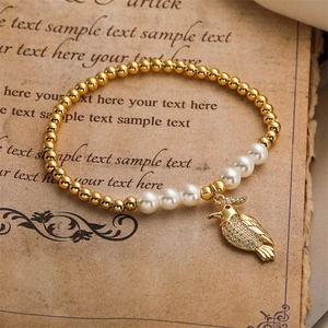 Détail d'un bracelet doré avec perles blanches et un charm perroquet en cristaux