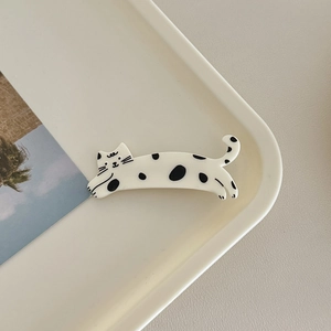 Detailed view of a black and white spotted cat hair clip on a minimalist cream tray