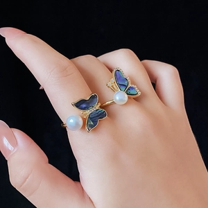 Detail of gold butterfly ring with pearl and blue shell inlay worn on a model's hand