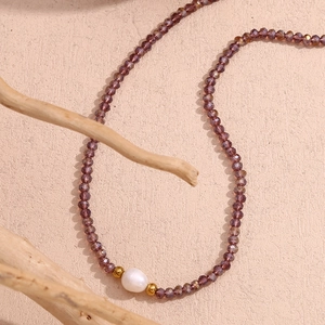 Detail of purple faceted crystal beads with a white pearl and gold accents on a textured surface