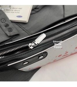 Detail of silver metal zipper puller on a white crossbody bag with red splatter pattern