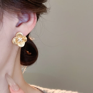 Close-up of elegant matte gold flower stud earrings with zircon inlay worn by a model