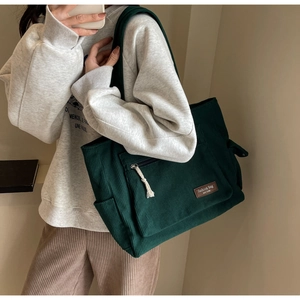 Detail of green corduroy tote bag showing ribbed texture and fashion label on front pocket