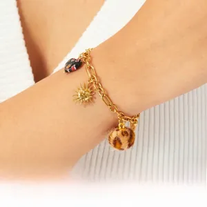 Detailed shot of gold bracelet with sun pendant, leopard heart charm, and plush ball