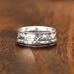 Macro detail of vintage silver mountain range ring with flying birds on wood background