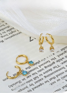 Macro shot of gold-plated titanium earrings with white and blue zircon on a book