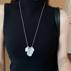 Detail of a silver chain necklace with three white petal-shaped resin pendants on a model