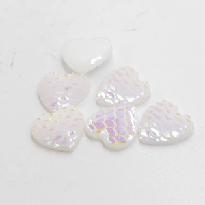 Macro view of white iridescent heart-shaped resin cabochons with mermaid scale texture