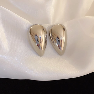 Macro detail of silver teardrop earrings with mirror-polished finish on white silk background