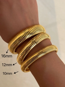 Three gold Tubogas stretch bracelets in 16mm, 12mm, and 10mm widths on a model's wrist