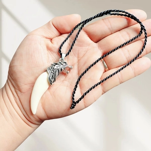 Wolf tooth resin pendant necklace with silver wolf head and black cord in hand