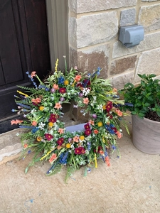 Outdoor view of a colorful faux wildflower wreath with vibrant silk ranunculus and greenery