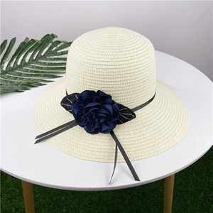 Detail of cream straw sun hat with large navy fabric flower and elegant ribbon