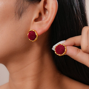 Close-up of red velvet geometric earrings with gold trim worn by a female model