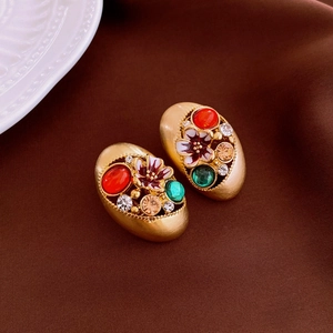 Detail of vintage enamel earrings with colorful gemstones on dark satin background
