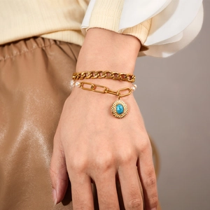 Close-up of layered gold chain bracelet with white pearls and blue turquoise pendant