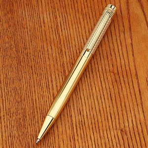 Detail of brass pen with grid textured cap resting on a professional wooden desk surface