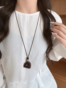 Close-up of wooden resin geometric pendant necklace worn on a white linen shirt