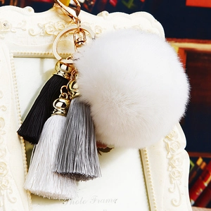 Macro detail of white faux fur pompom keychain with tricolor tassels and gold hardware