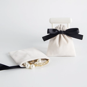 Detail of cream velvet jewelry pouch with black silk ribbon bow and pearl necklace