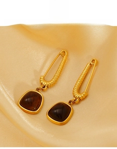 Macro detail of gold-plated titanium steel earrings with square stones on satin fabric
