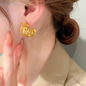 Close-up of a gold multi-strand twisted C-shaped earring on model with metallic finish
