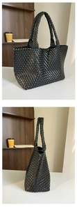 Detail view of large black woven tote bag showing premium leather texture and handle design