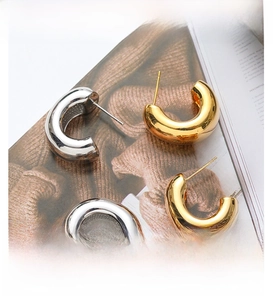 Macro detail of gold and silver C-shaped chunky hoop earrings on a magazine background