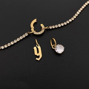 Detail view of gold tennis bracelet with gothic 'y' letter and crystal pendant charms.