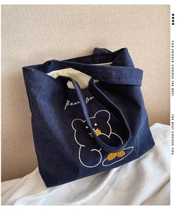 Detail of navy blue corduroy tote bag featuring an embroidered cartoon bear on plush surface