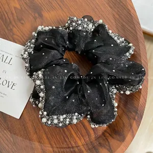 Macro detail of black organza scrunchie with rhinestones and faux pearls on wood