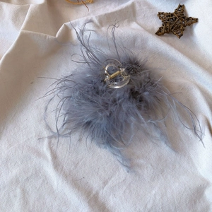Top view of a transparent hair claw clip with grey ostrich feathers on linen background