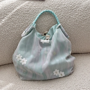 Detail of green floral lace embroidery on sheer fabric handbag with woven handles