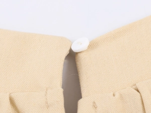 Close-up of beige textured fabric featuring a white round button on the neckline
