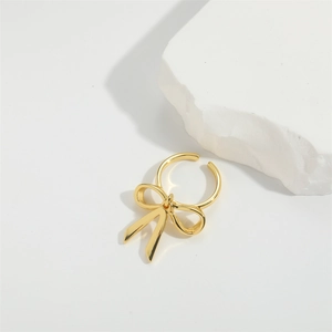 Detail of elegant gold bow-shaped open ring with high-gloss finish on a white stone base