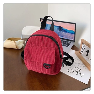 Detail of red corduroy mini backpack on wooden desk with flowers and aesthetic props