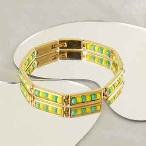 Detail of gold beaded bracelet with alternating yellow and green beads on a mirror surface