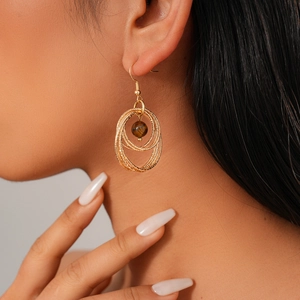Close-up of golden multi-layer geometric hoop earrings with brown tiger eye beads on a model