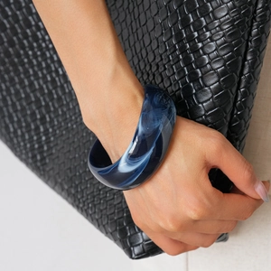 Detail of dark blue marble pattern acrylic bangle on wrist with woven background