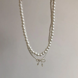Detail of double-layer pearl necklace with sparkling rhinestone bow pendant and water drop charms