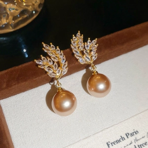 Close-up of golden wheat zircon stud earrings with large champagne pearls on velvet box