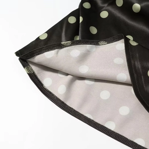 Detailaufnahme von schwarzem Satin-Stoff mit hellgrünen Punkten und feiner Naht