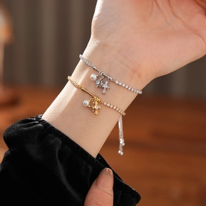 Detail of zircon cross and pearl bracelets in gold and silver finish on model's wrist