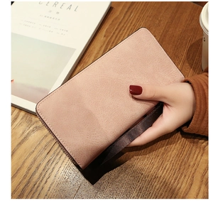 Pink long faux leather wallet with silver zipper and wrist strap on wooden table