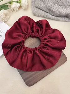 Close-up of a burgundy jacquard satin scrunchie with rose patterns on a wooden tray