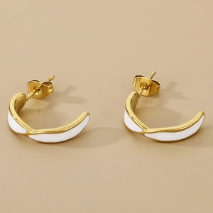 Detailed close-up of wavy C-shaped gold earrings with white enamel on a tan background