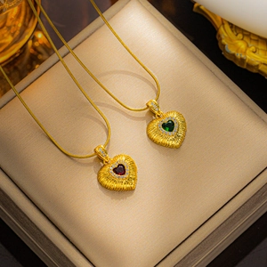 Close-up of 18k gold heart pendants with red and green emerald zircons on snake chains
