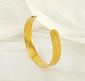 Détail d'un bracelet jonc plaqué or en acier inoxydable avec texture martelée sur soie blanche