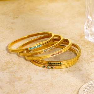 Set of gold stainless steel bracelets with colorful zircon stones on stone background