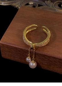 Close-up of gold plated layered ring with zircon pavé and hanging pearl tassels
